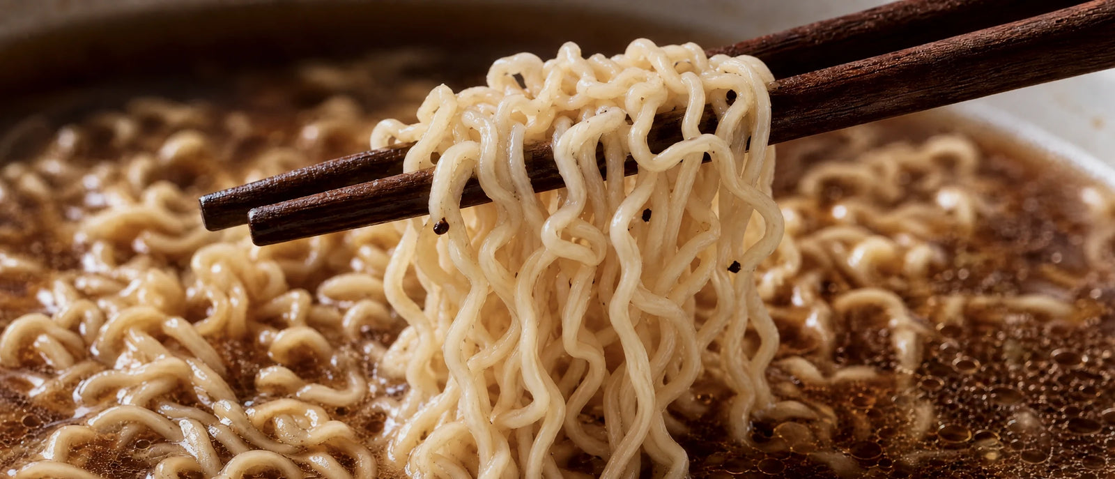 A close look at NOMI noodles lifted steaming from a dark broth