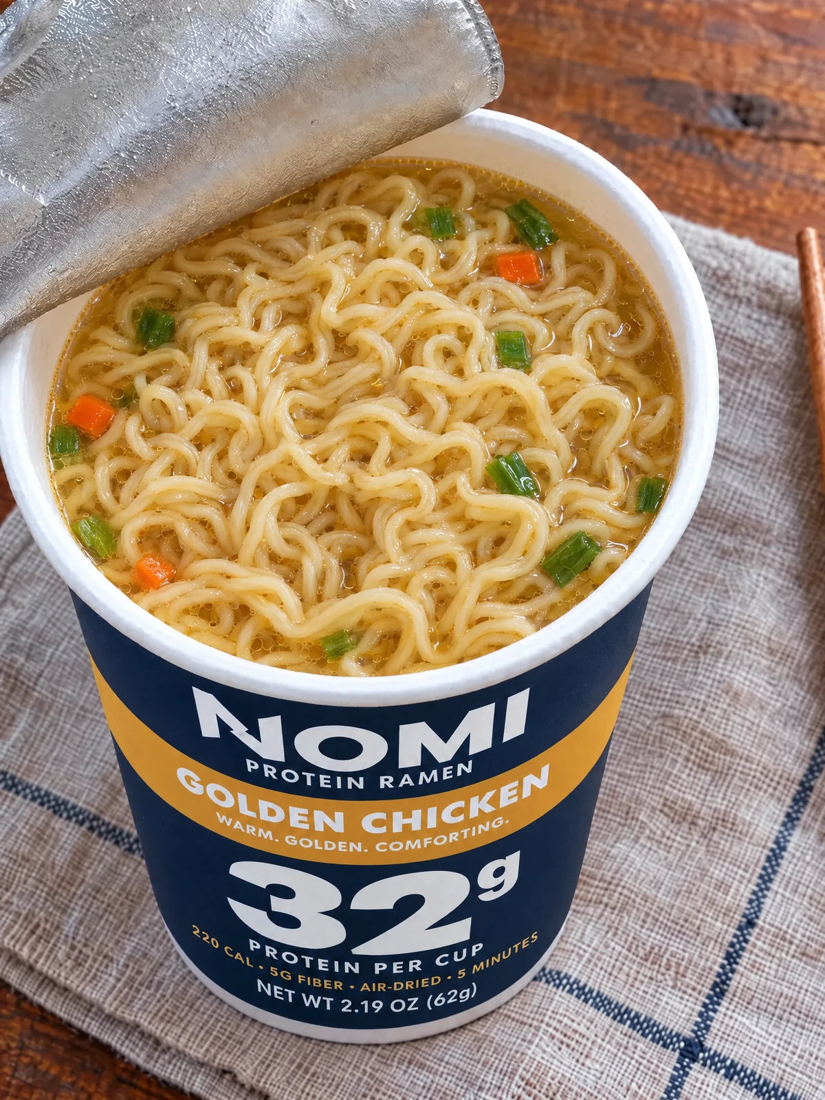 An open NOMI Golden Chicken cup, noodles in clear golden broth with carrot and scallion