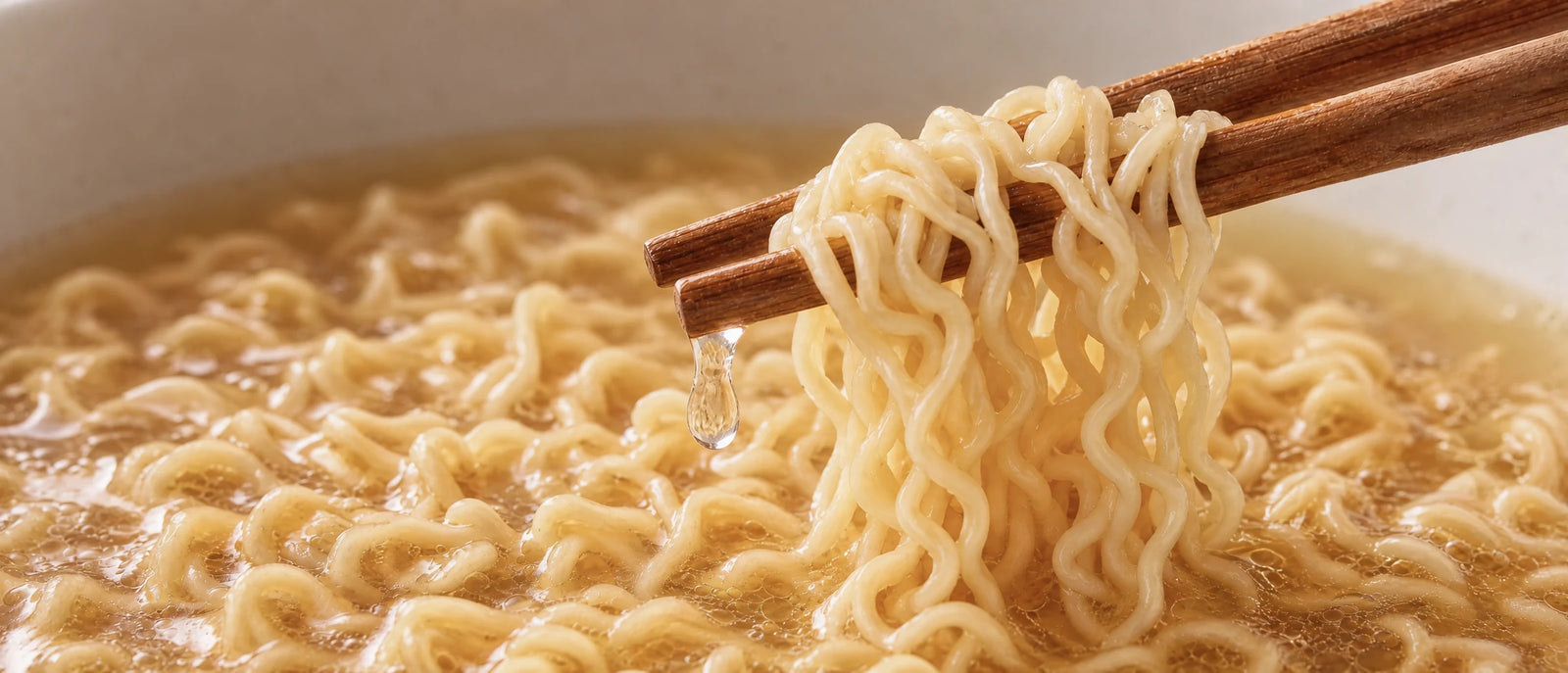 A close look at NOMI noodles lifted steaming from a golden broth
