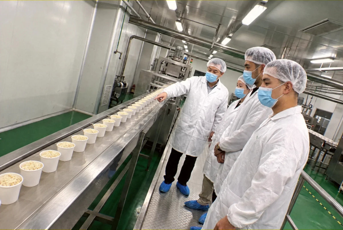 Alain on the line at the factory in China, the plant manager walking him along a conveyor of filled noodle cups
