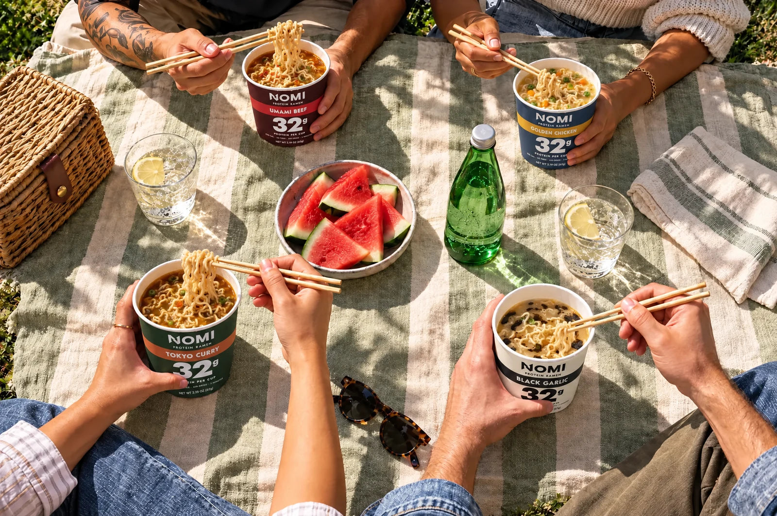 Friends eating NOMI cups on a picnic blanket in the park